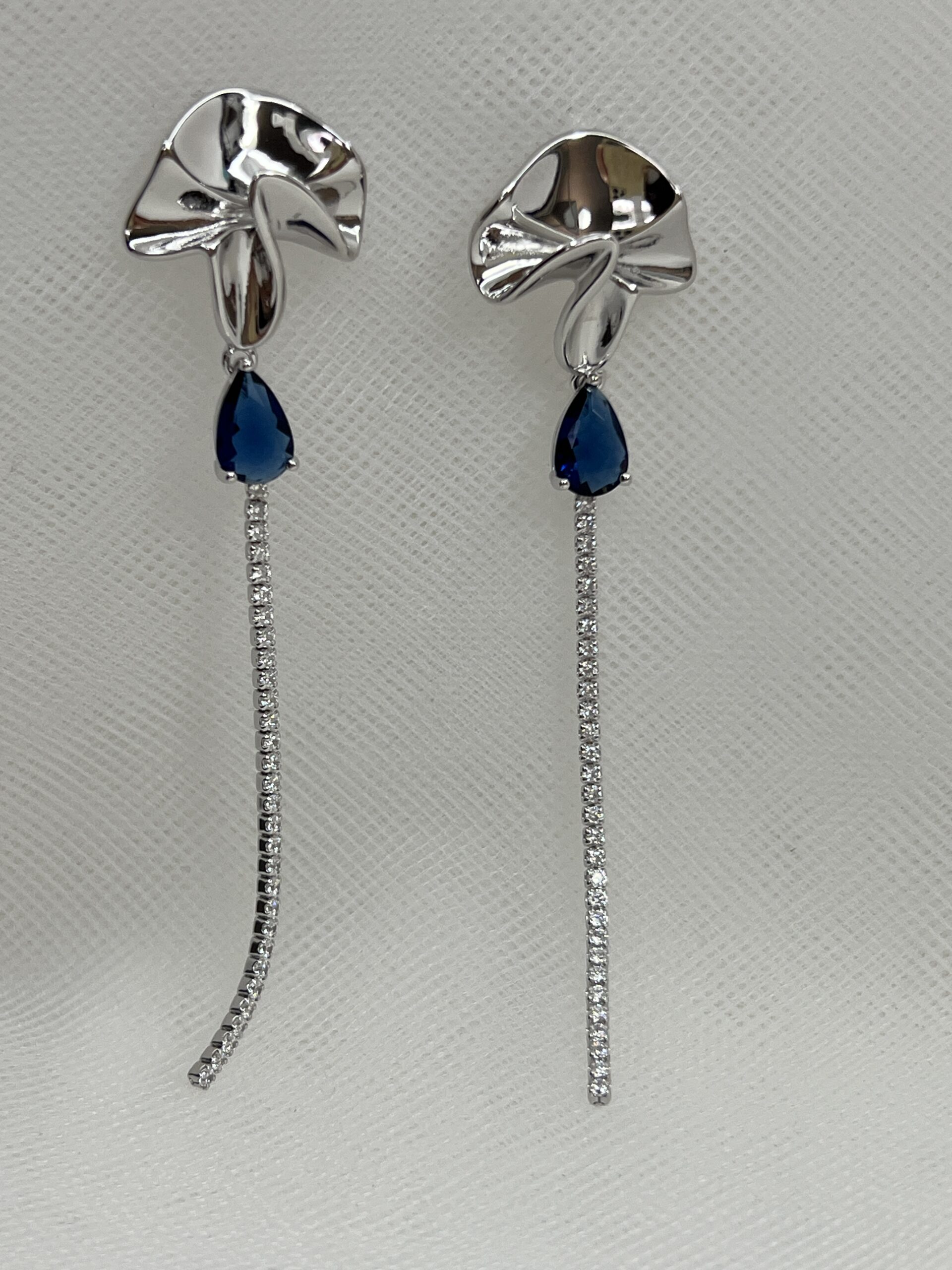 Pendientes largos de plata rodiados en oro blanco boton con formas onduladas y cadena de circonitas con piedra azul.
